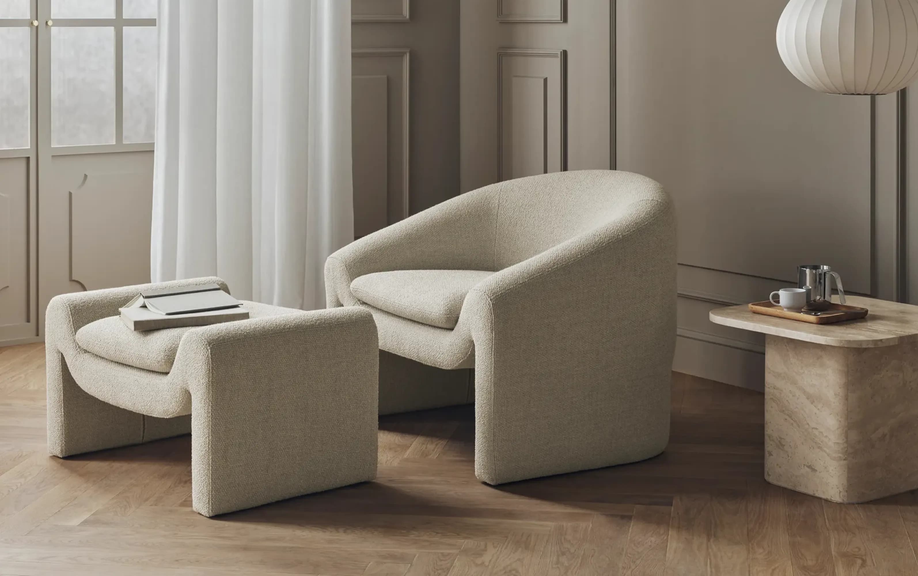 Elegant reading corner with beige armchair and matching ottoman, minimalist wooden side table, and soft natural light filtering through sheer curtains.
